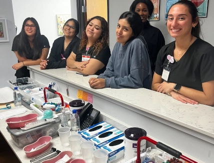 medical assistant students standing at clinic desk in front of medical supplies